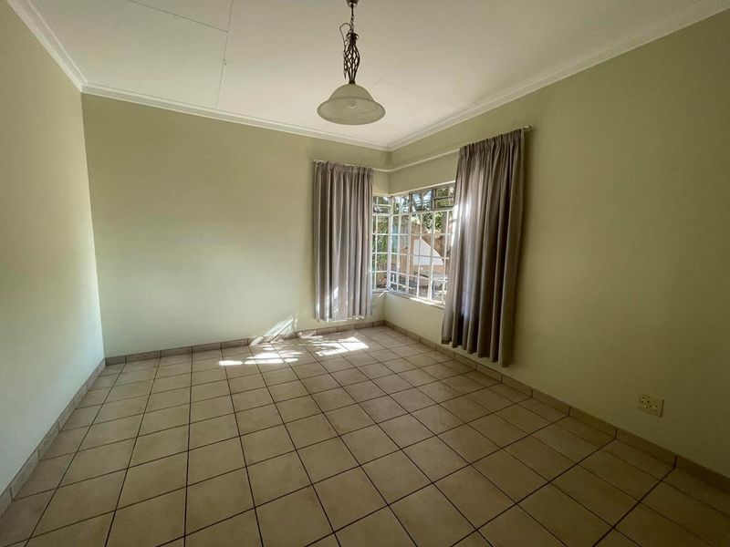 An empty living room featuring neutral tiled flooring, a corner window with natural light, and a central pendant light fixture.