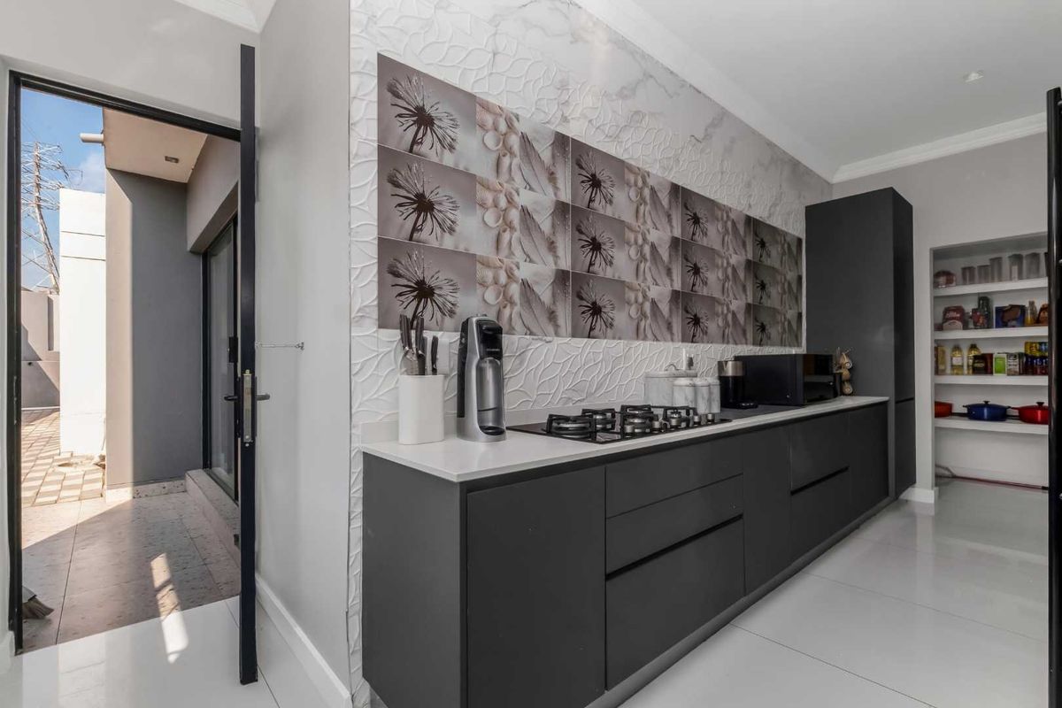 Modern kitchen featuring dark cabinetry, stone countertops, a gas hob, and a convenient walk-in pantry, with direct access to an outdoor patio area.