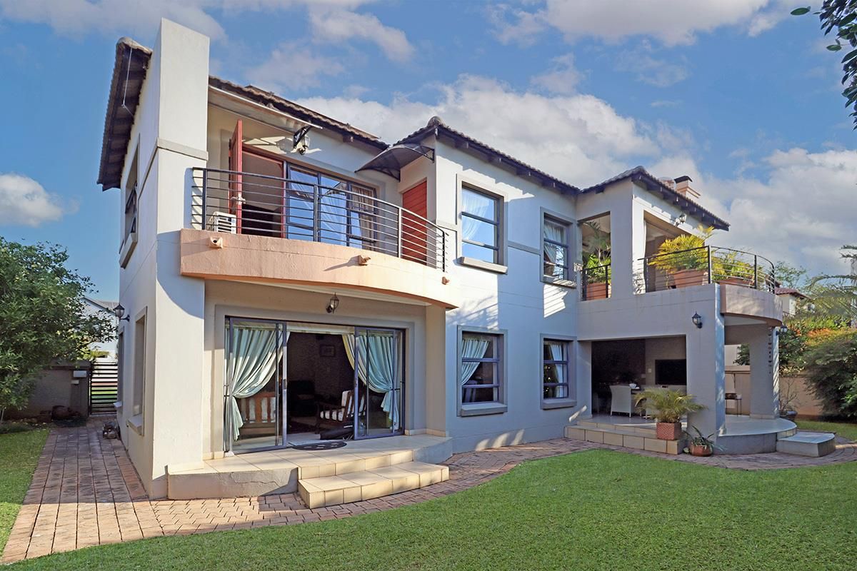 Rear view of a two-story house featuring a covered patio, upper-level balcony with metal railings, and a landscaped garden with paved walkways.