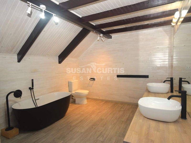 Modern attic-style bathroom featuring exposed timber beams, a sleek freestanding bathtub, and a double vanity with vessel sinks.
