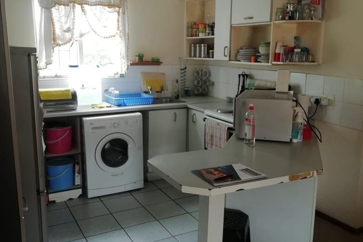 A compact kitchen featuring tiled flooring, built-in cabinetry, a breakfast bar, and integrated laundry plumbing, offering a functional layout for an apartment.
