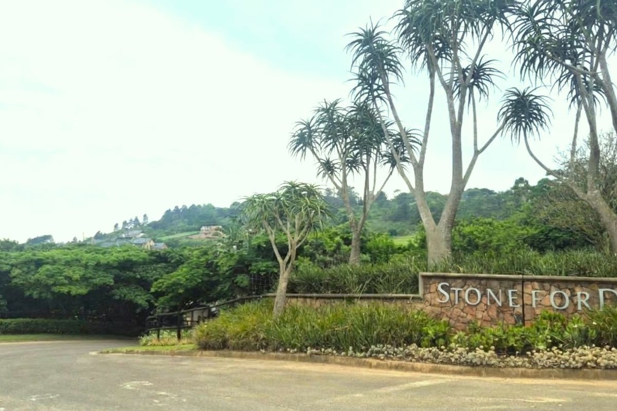 Entrance view of Stoneford estate featuring a stone signage wall, mature trees, and landscaped gardens along a paved road.