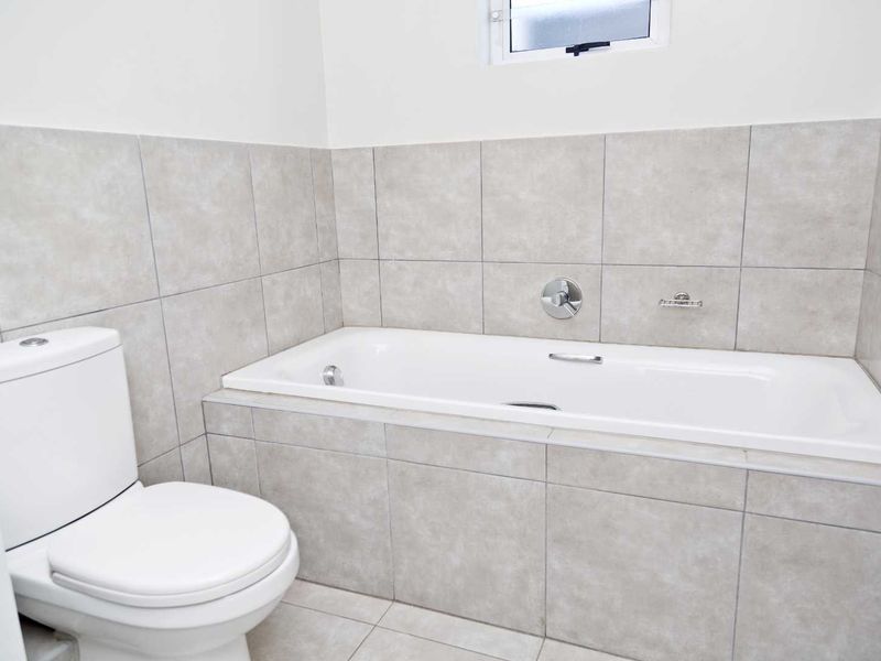 A clean, modern bathroom featuring a built-in bathtub, tiled walls and flooring, and a standard toilet.