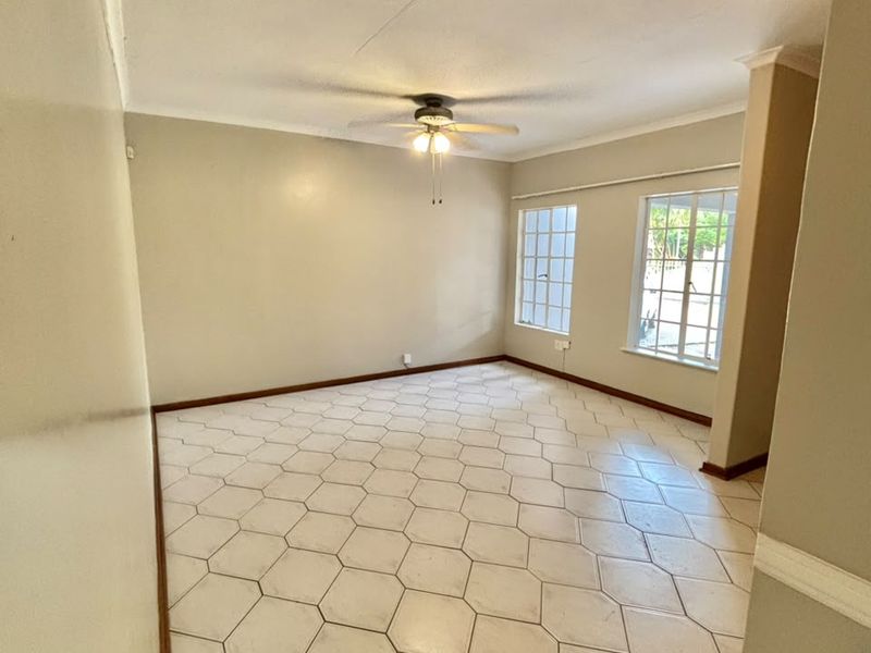 A bright, empty living room featuring neutral walls, large grid windows, and distinctive hexagonal floor tiles, offering a clean canvas for interior design.