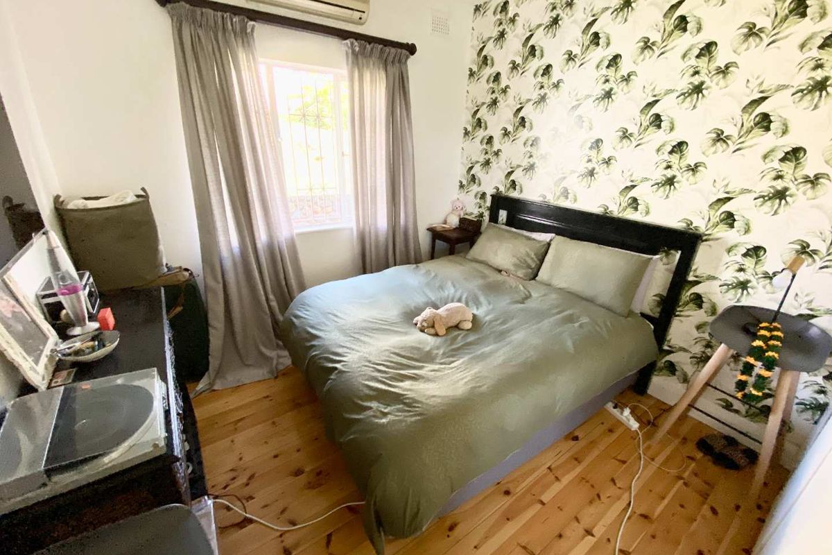 A cozy bedroom featuring polished timber flooring, a decorative feature wall, and a wall-mounted air conditioning unit.