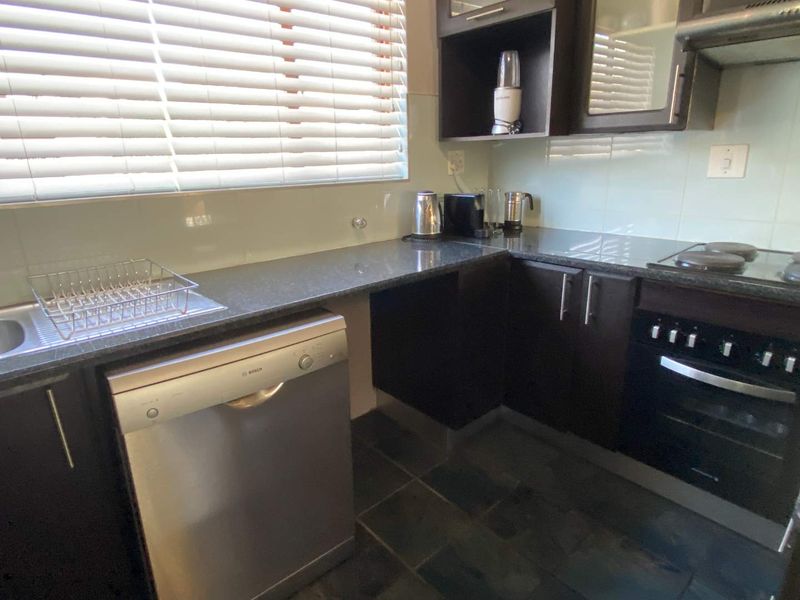 Compact kitchen featuring dark cabinetry, granite countertops, built-in oven, electric hob, and a tiled splashback with natural light from the window.