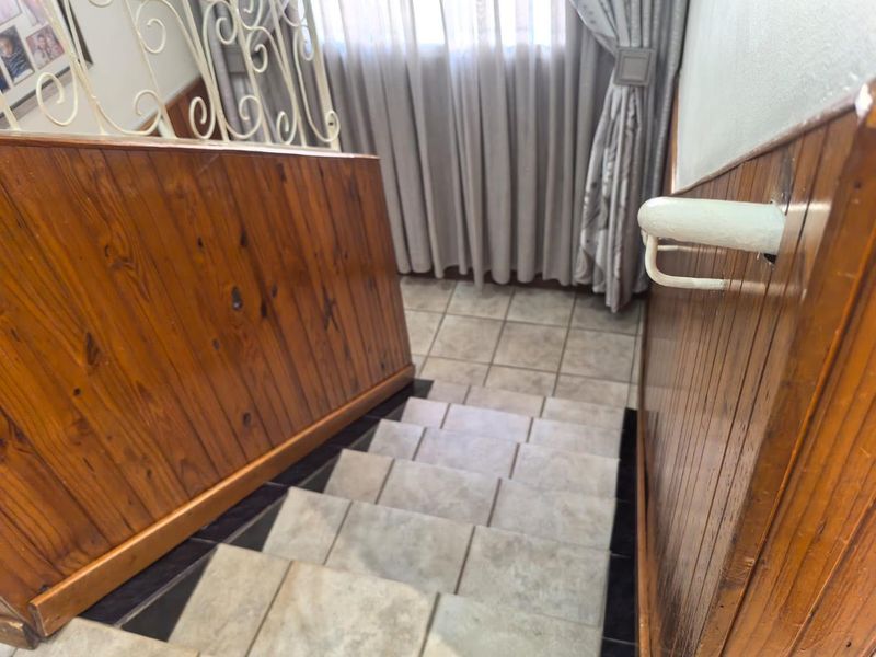 A staircase featuring tiled steps, wooden wall paneling, and a decorative wrought iron balustrade leading to a lower level.