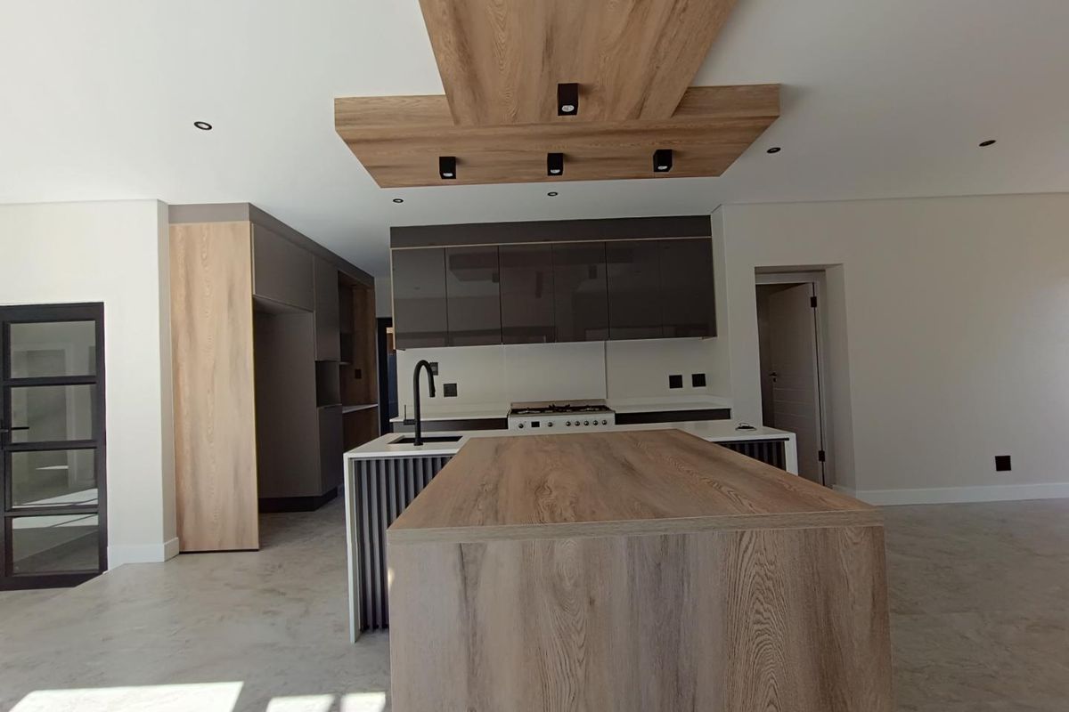 Modern open-plan kitchen featuring a large central island, wood-grain cabinetry, integrated gas hob, and a stylish suspended ceiling feature with recessed lighting.