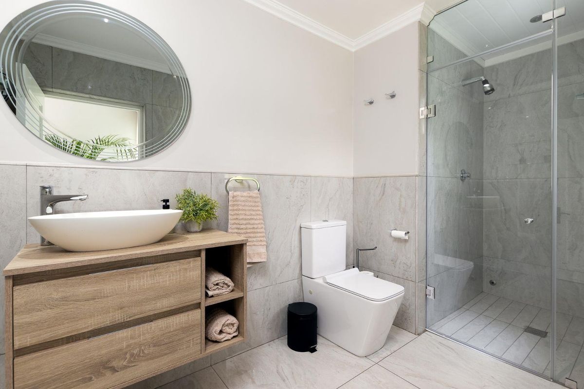 Modern bathroom featuring a floating wood-look vanity with a vessel sink, a glass-enclosed walk-in shower, and neutral floor-to-ceiling tiling.