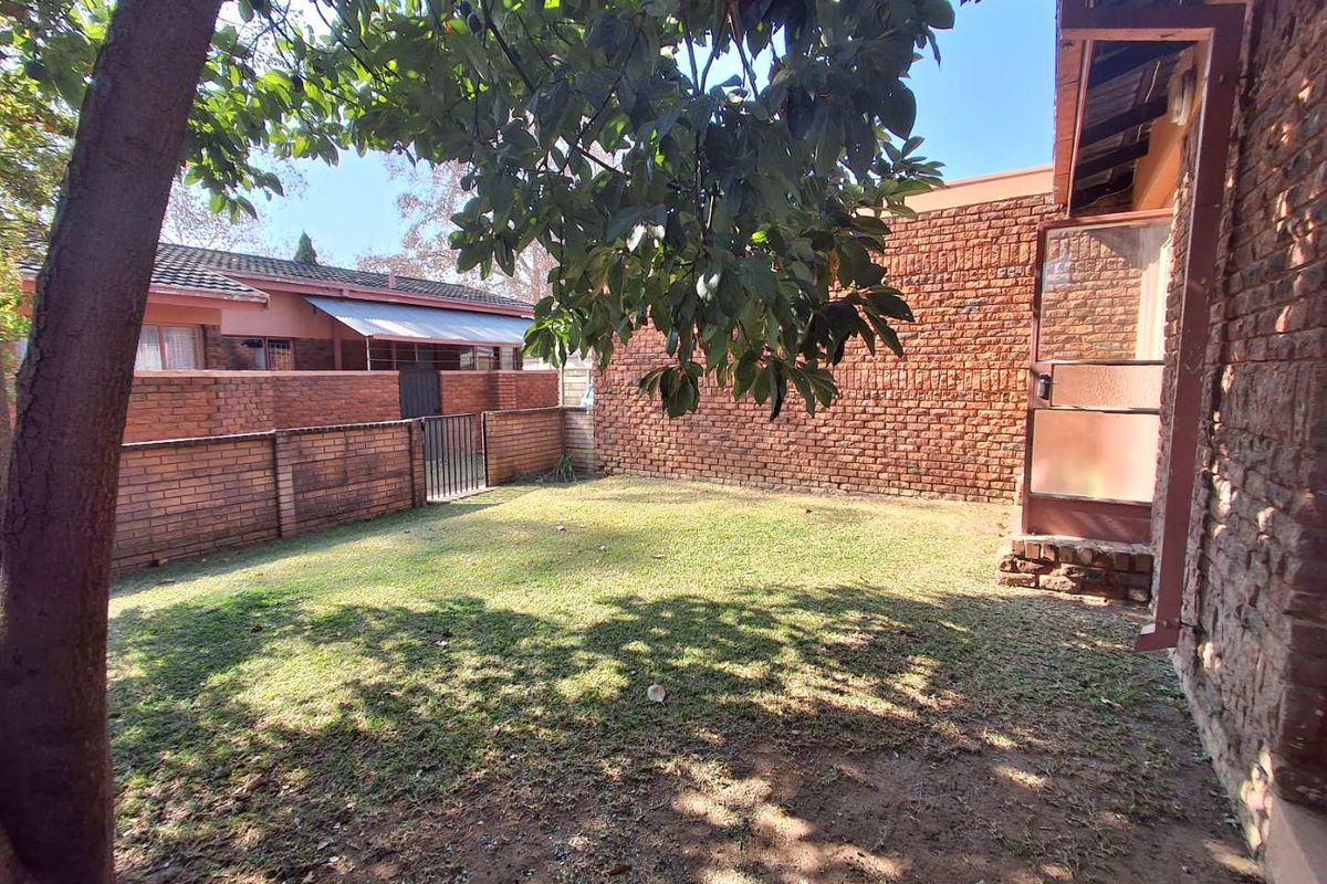 A private rear garden area featuring a lawn, enclosed by traditional brick boundary walls and a metal access gate.