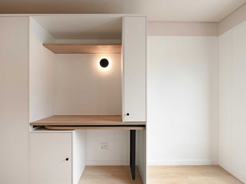 A modern, minimalist bedroom featuring custom built-in cabinetry with an integrated desk, shelving, and sleek lighting.