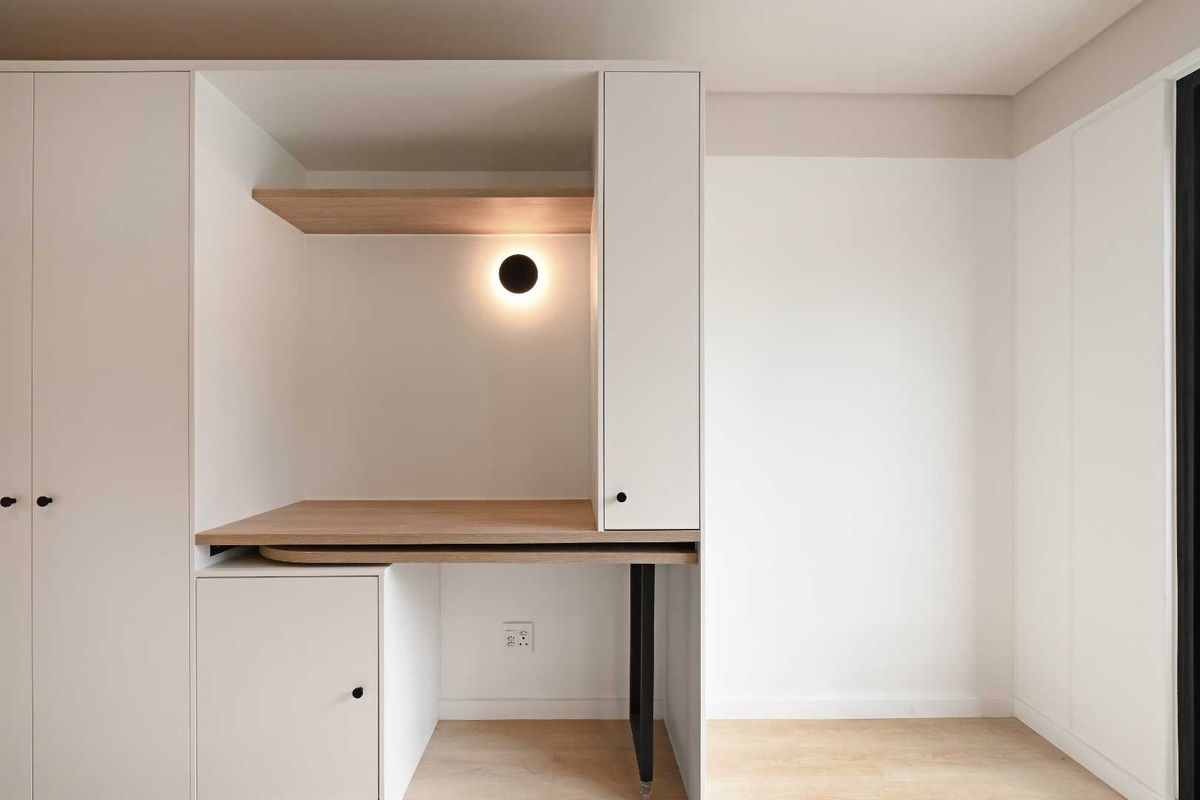 A modern, minimalist bedroom featuring custom built-in cabinetry with an integrated desk, shelving, and sleek lighting.