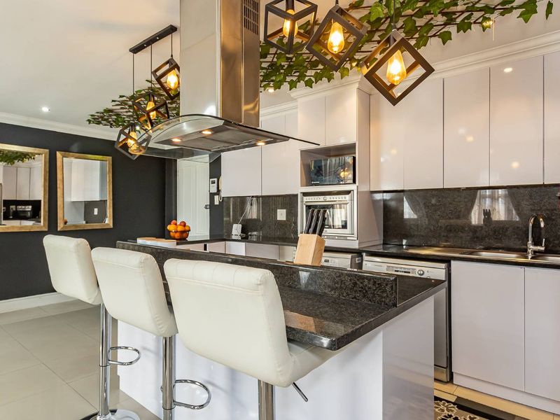 Modern kitchen featuring high-gloss cabinetry, granite countertops, stainless steel appliances, and a breakfast bar with integrated lighting.