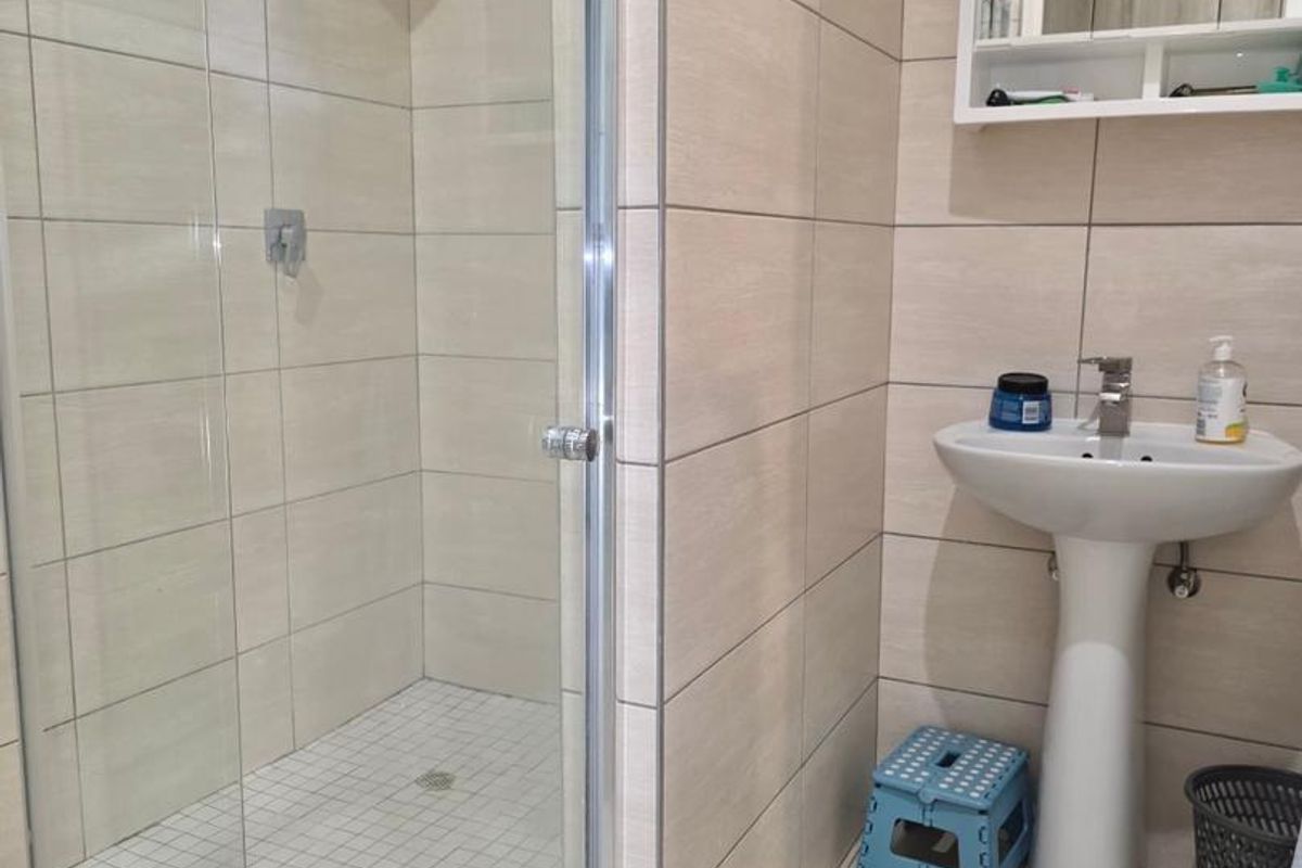 A modern bathroom featuring a glass-enclosed shower with tiled walls and a pedestal basin with a wall-mounted mirrored cabinet.