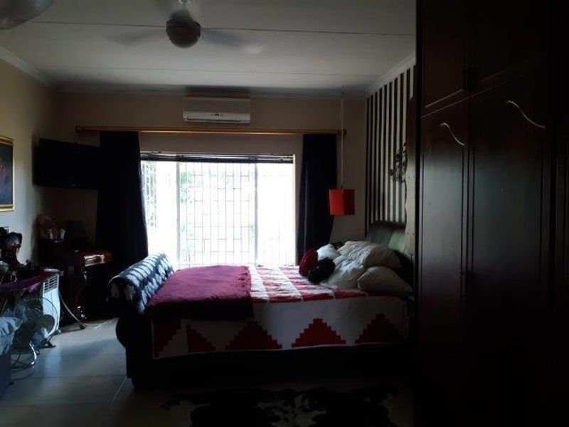 A bedroom featuring a ceiling fan, wall-mounted air conditioning unit, and built-in wardrobe, with security bars installed on the window.