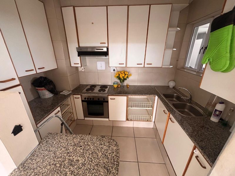 A functional kitchen featuring granite countertops, built-in cabinetry, an electric hob, oven, extractor fan, and a double bowl sink with tiled finishes.