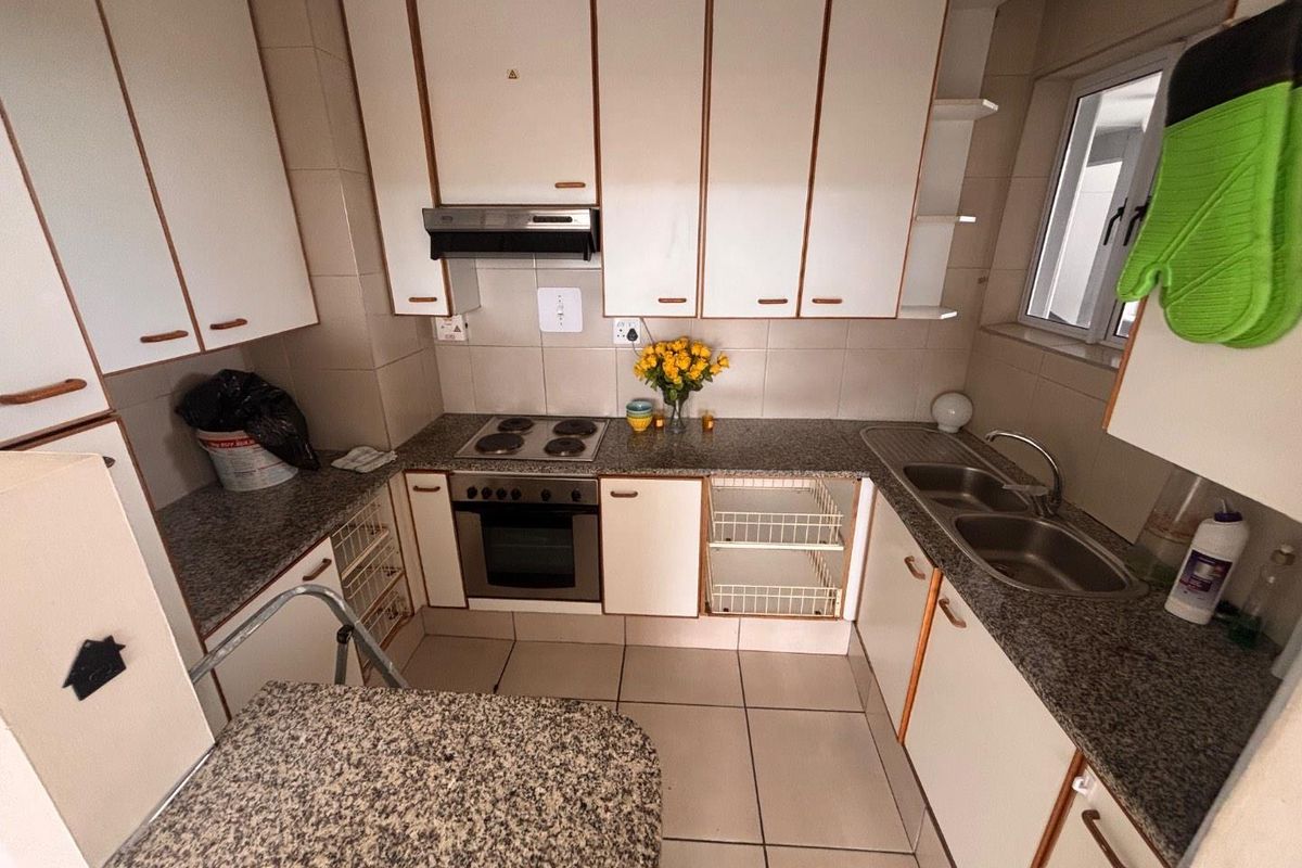 A functional kitchen featuring granite countertops, built-in cabinetry, an electric hob, oven, extractor fan, and a double bowl sink with tiled finishes.