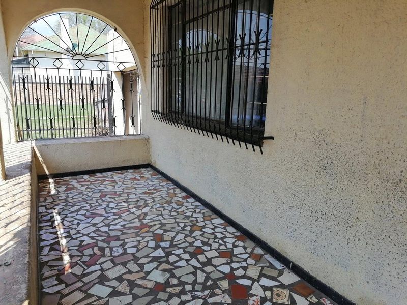 A covered patio area featuring an arched entrance, security bars on the windows, and traditional crazy paving flooring.