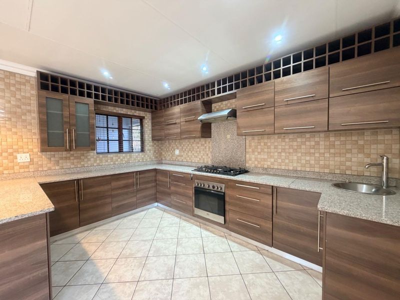 A spacious, well-maintained kitchen featuring extensive wood-finish cabinetry, granite countertops, a gas hob, built-in oven, and integrated wine storage.