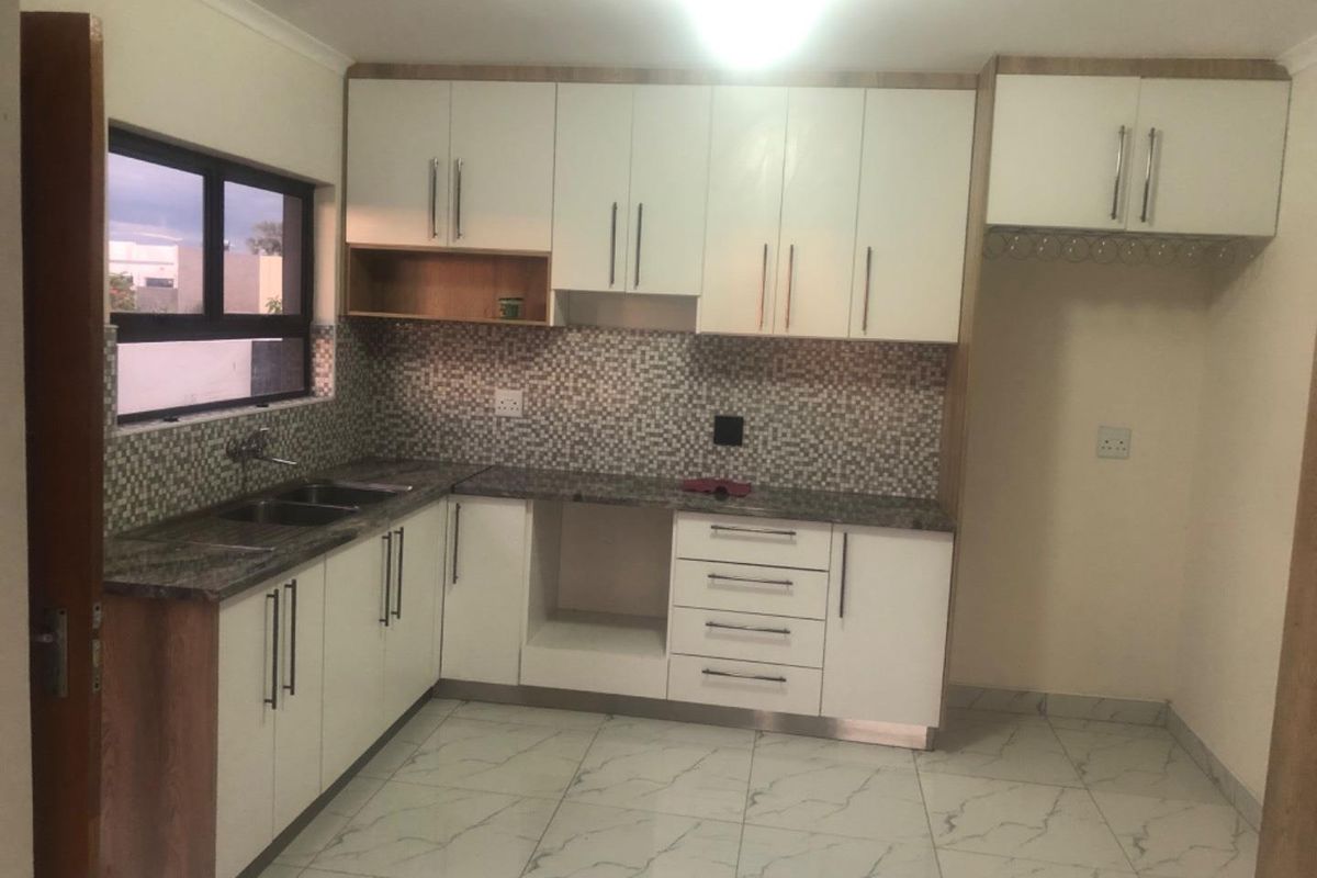 Modern kitchen featuring white cabinetry, granite countertops, mosaic tile backsplash, and marble-look floor tiles with ample storage and dedicated appliance space.