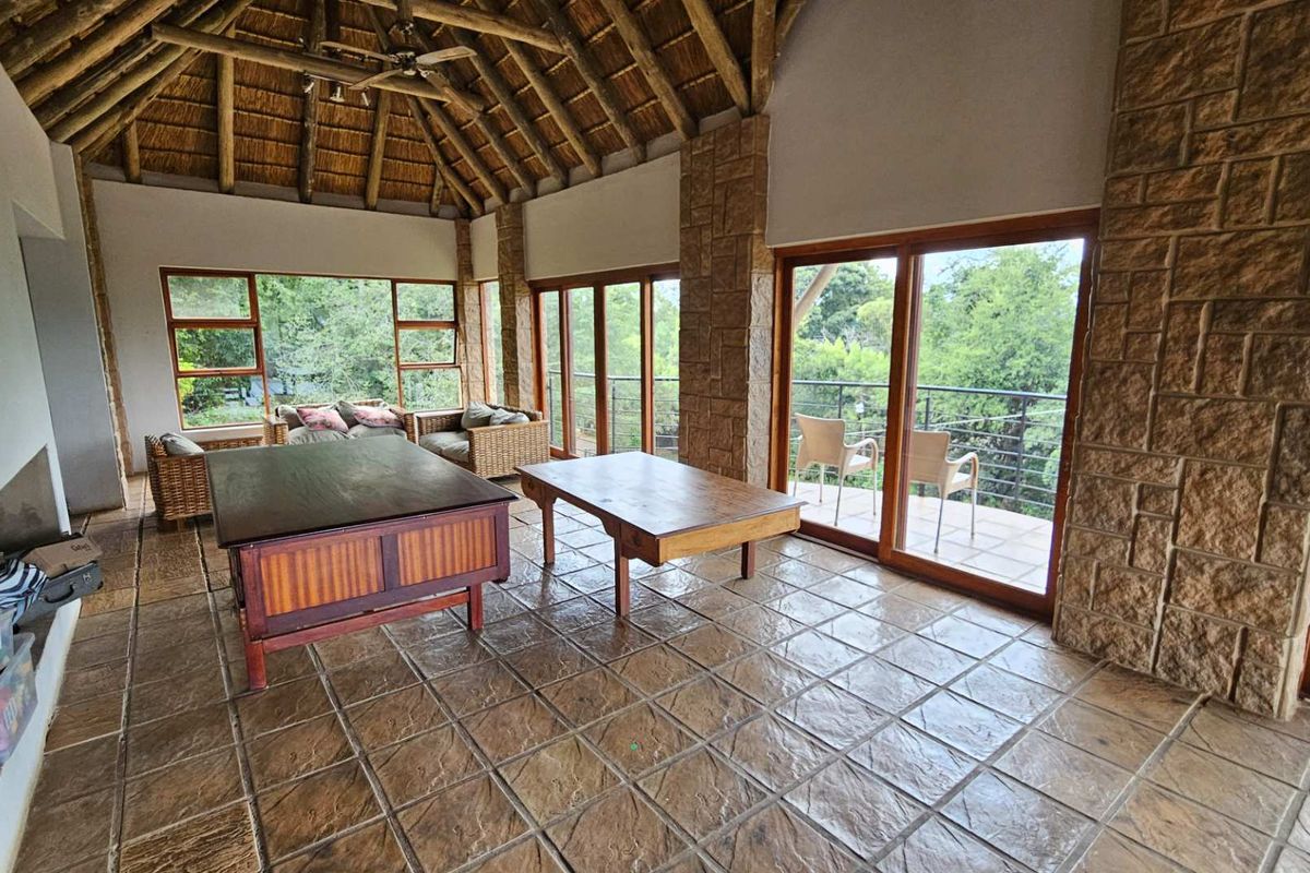 Spacious living area featuring a high vaulted thatched ceiling, exposed stone pillars, tiled flooring, and large sliding glass doors opening to a balcony.