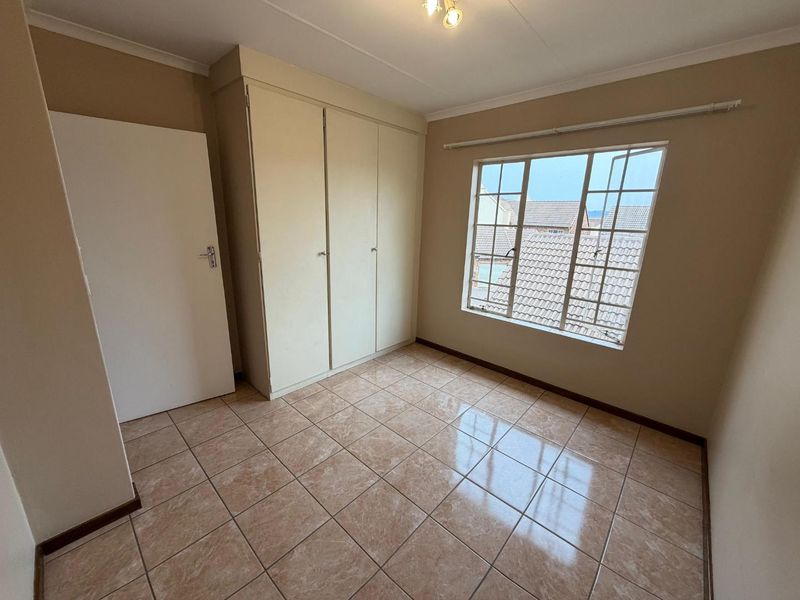 A clean, empty bedroom featuring tiled flooring, built-in cupboards, and a window with security bars, offering a neutral space ready for personalization.