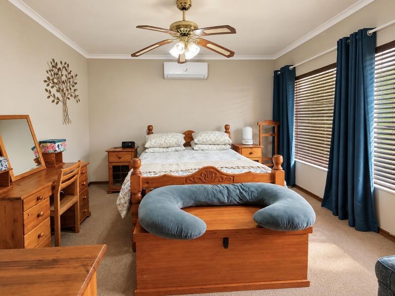 A well-maintained bedroom featuring carpeted flooring, a ceiling fan, and a wall-mounted split-system air conditioner for climate control.