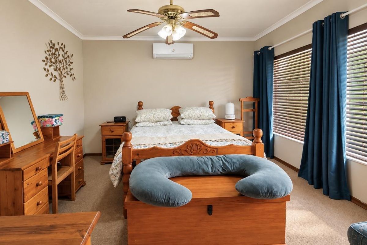 A well-maintained bedroom featuring carpeted flooring, a ceiling fan, and a wall-mounted split-system air conditioner for climate control.