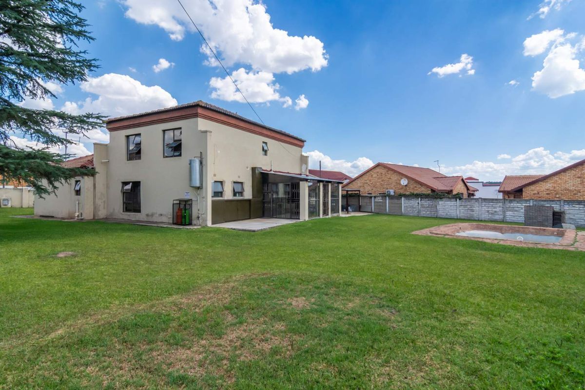 Rear view of the property featuring a spacious lawn, a covered patio area, and a swimming pool with a concrete surround.