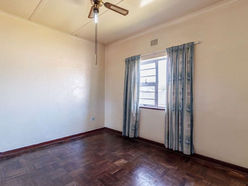 An empty bedroom featuring original parquet flooring, a ceiling fan, and a louver window with neutral wall finishes.