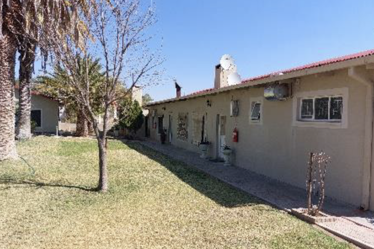 Rear view of the property showing a paved walkway, lawn area, and exterior building features including roof and wall-mounted fixtures.