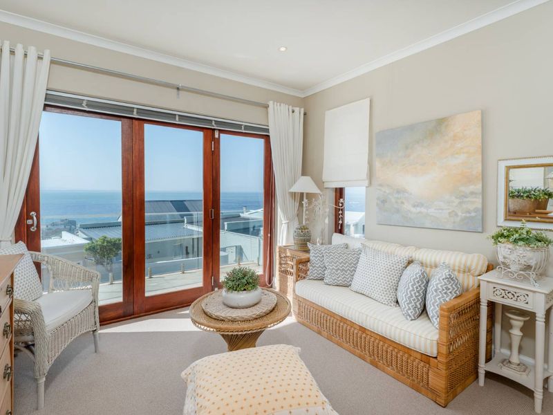 A bright living room featuring timber-framed sliding doors that open to a scenic ocean view, complemented by neutral carpeting and recessed lighting.