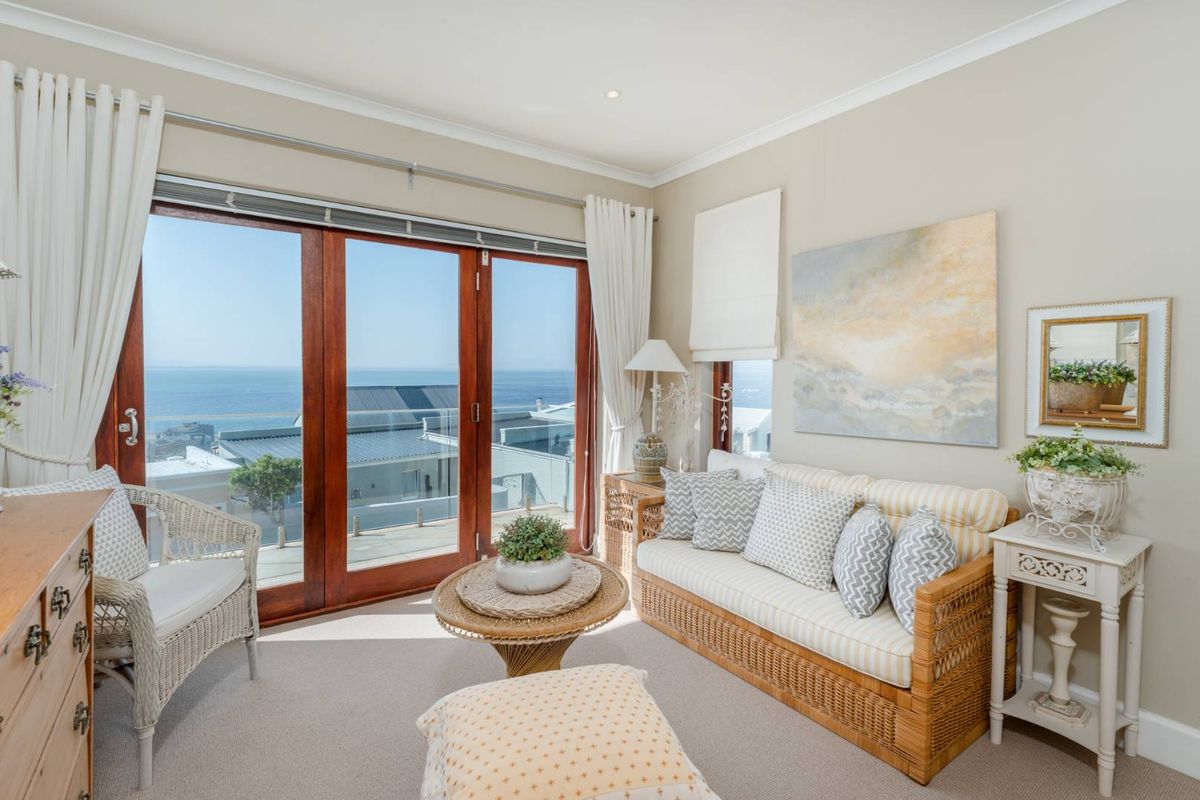 A bright living room featuring timber-framed sliding doors that open to a scenic ocean view, complemented by neutral carpeting and recessed lighting.