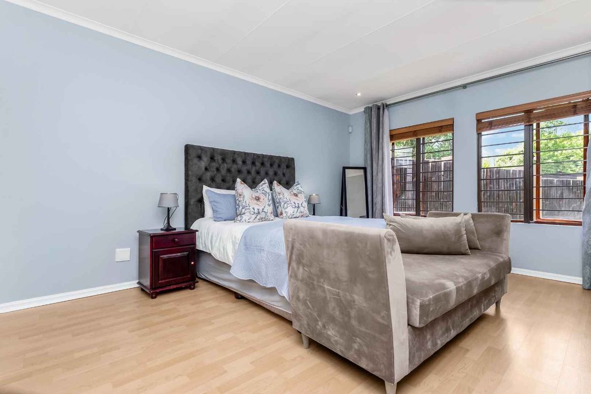 A well-maintained bedroom featuring light laminate flooring, soft blue walls, and large windows fitted with security bars.