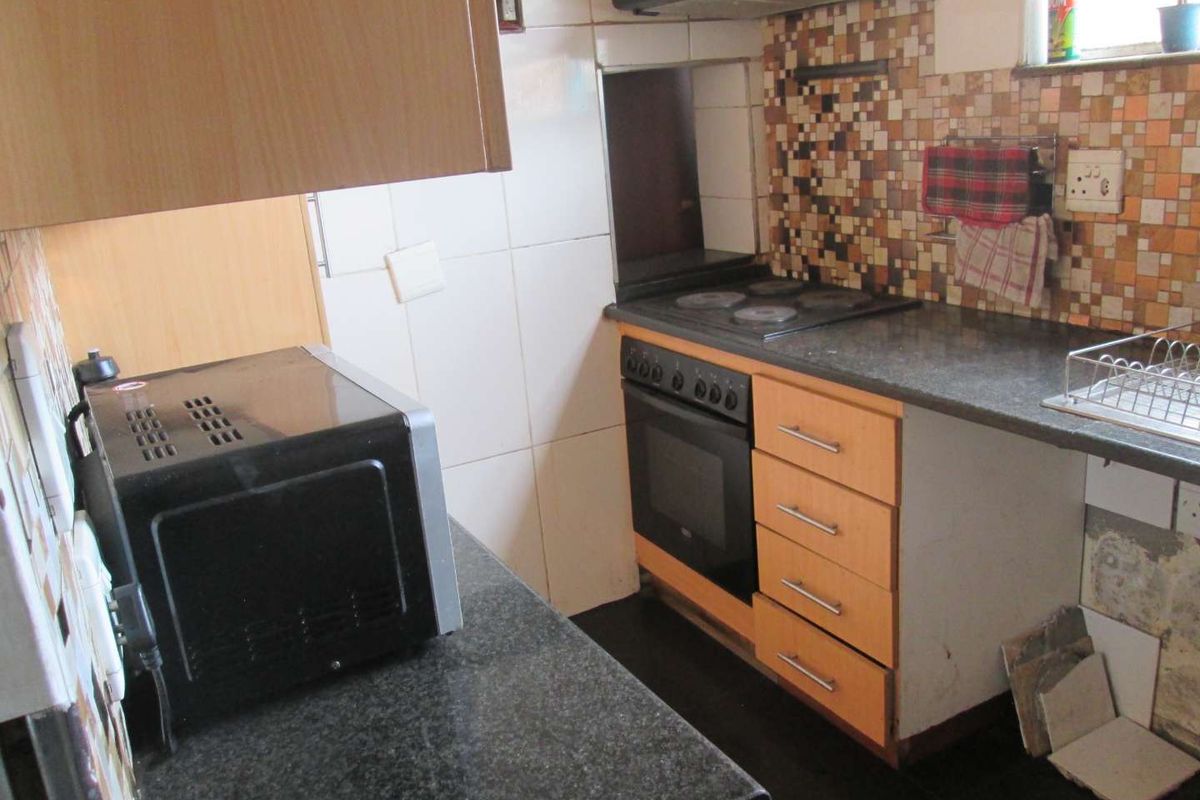 A compact kitchen featuring dark granite countertops, built-in oven and hob, extractor fan, and mosaic tile splashback with dated cabinetry.