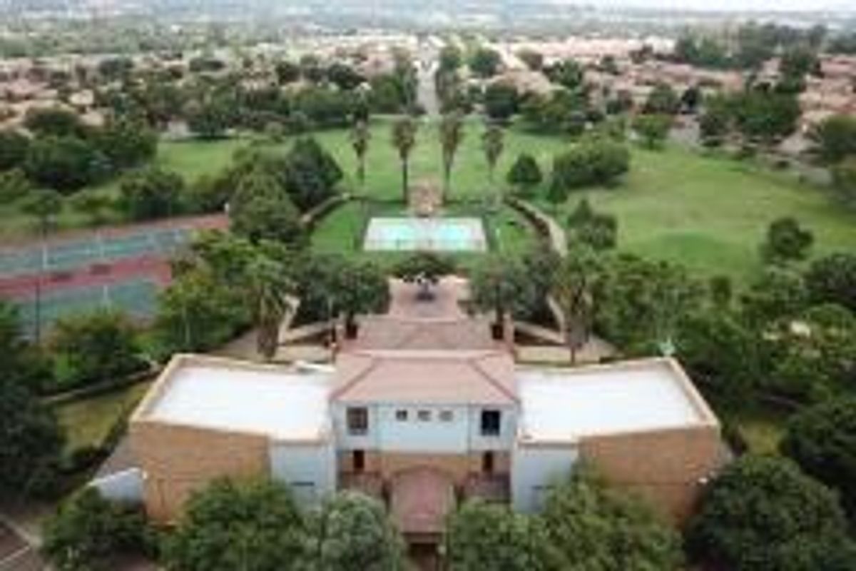 Aerial view of the property complex featuring landscaped grounds, a swimming pool, and tennis courts within a residential estate setting.
