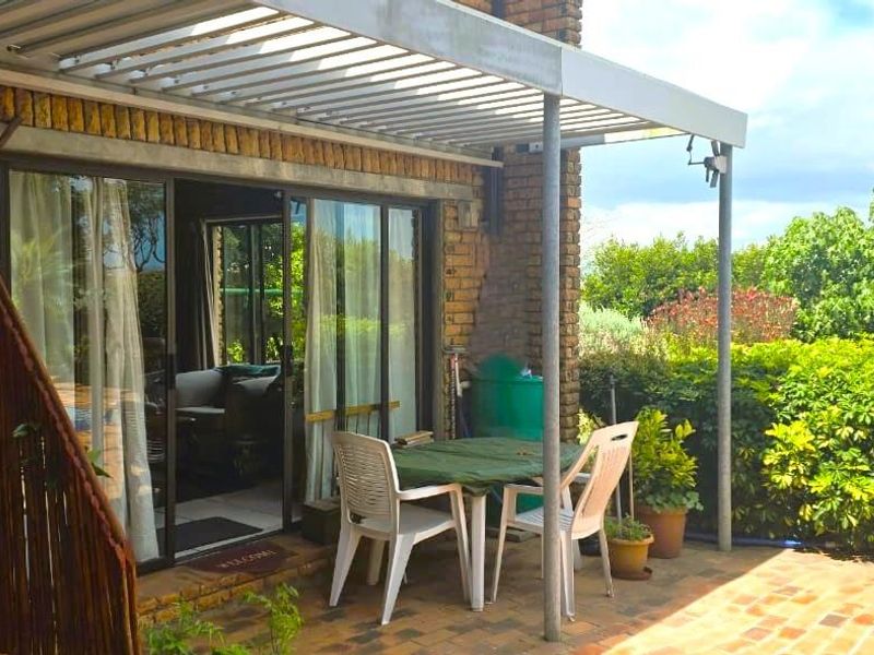 Covered patio area featuring a louvered roof, brick paving, and direct access to the interior through sliding glass doors.