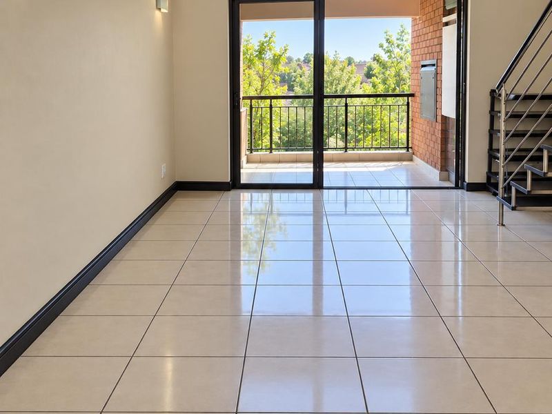 Spacious, light-filled living area featuring polished tile flooring, a modern staircase, and direct access to a private balcony through large sliding glass doors.