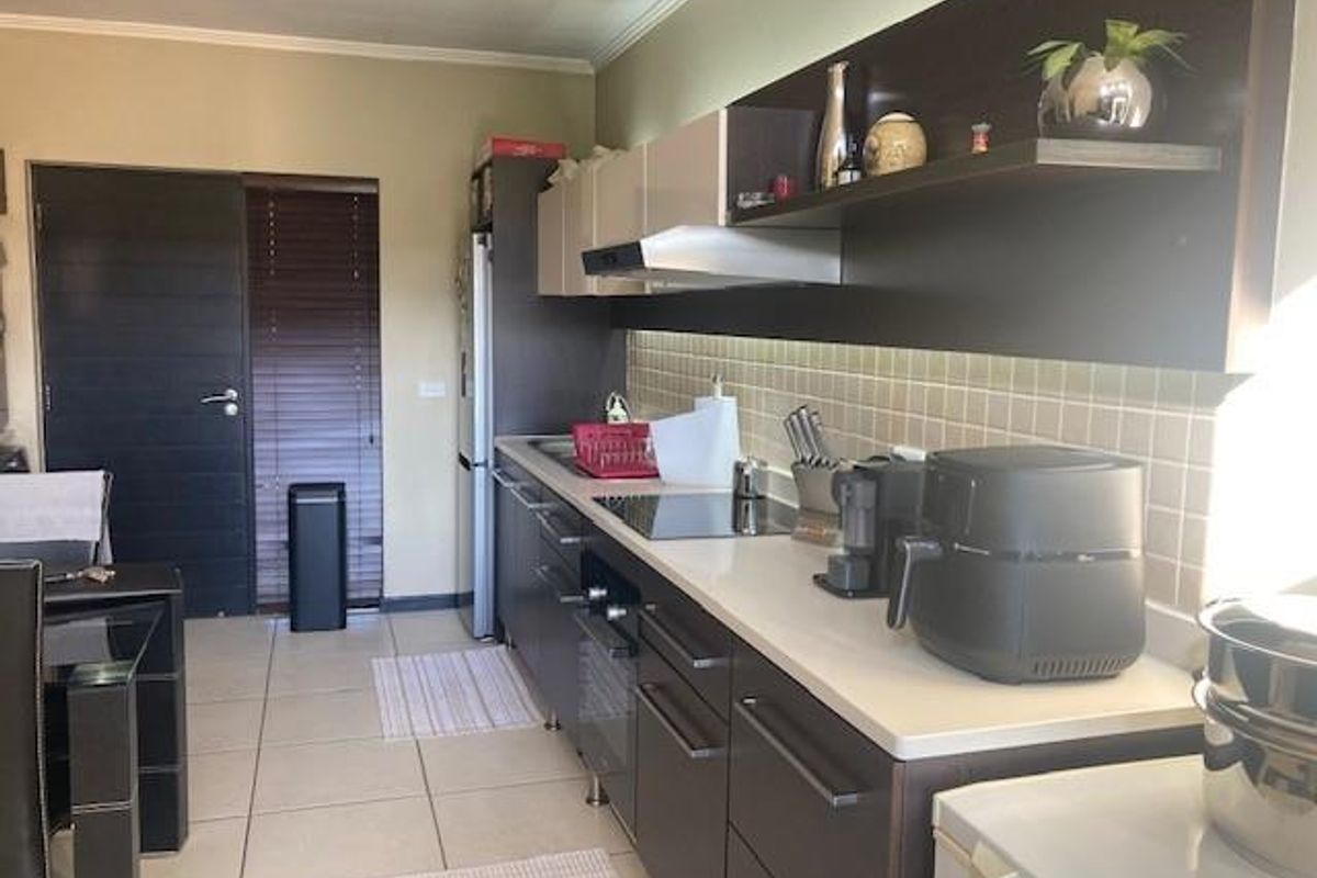 A modern galley-style kitchen featuring dark cabinetry, light countertops, a tiled backsplash, and integrated stainless steel appliances.