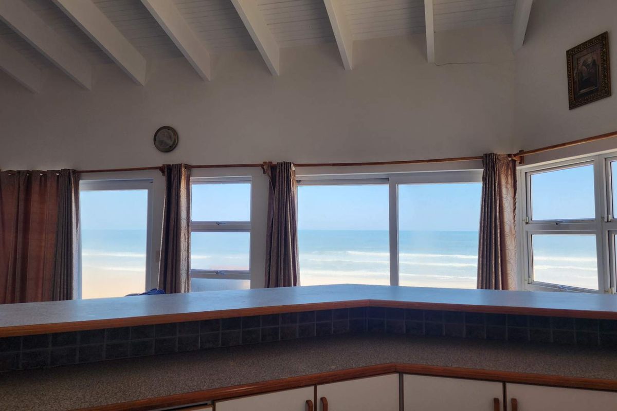 Kitchen area featuring built-in cabinetry and tiled countertops, with expansive ocean views through large sliding glass doors and windows.