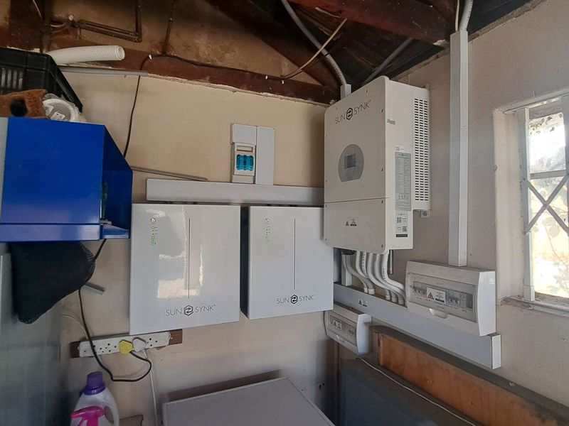 Utility area featuring a wall-mounted solar inverter and dual battery storage system with an integrated electrical distribution board.