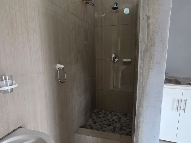 A bathroom featuring a walk-in shower with tiled finishes and a small vanity cabinet, currently showing signs of incomplete construction and unfinished wall surfaces.