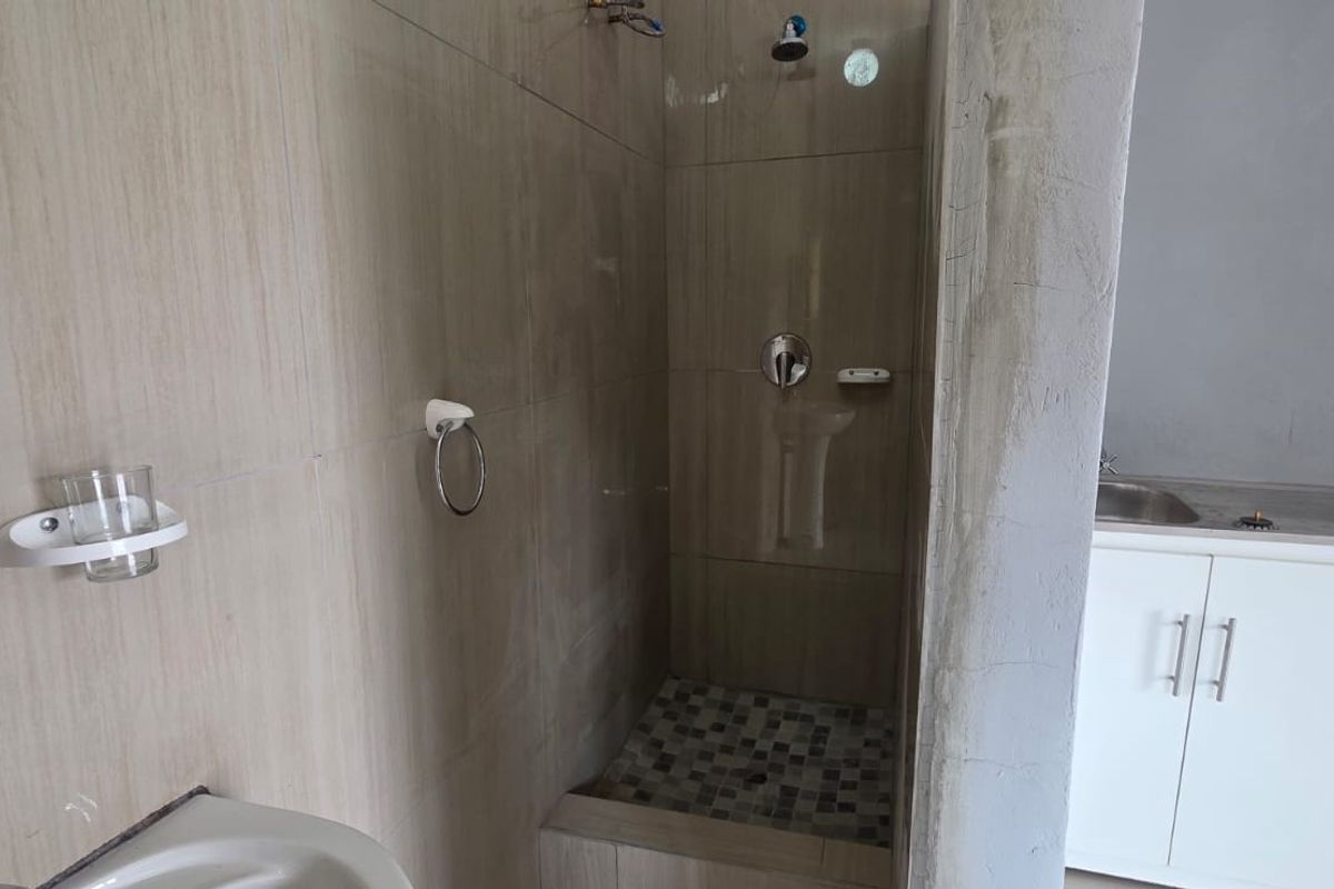 A bathroom featuring a walk-in shower with tiled finishes and a small vanity cabinet, currently showing signs of incomplete construction and unfinished wall surfaces.