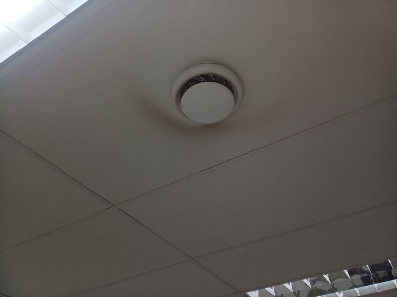 A view of a suspended office ceiling featuring an air conditioning vent with visible staining and a recessed fluorescent light fixture.