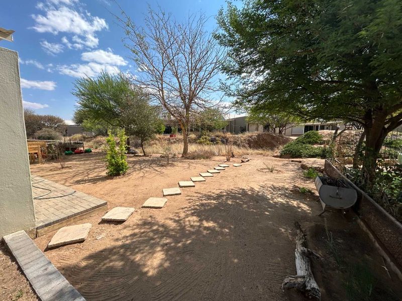 A spacious backyard garden featuring a paved patio area, stone stepping stones, and mature trees, offering potential for landscaping and outdoor improvement.