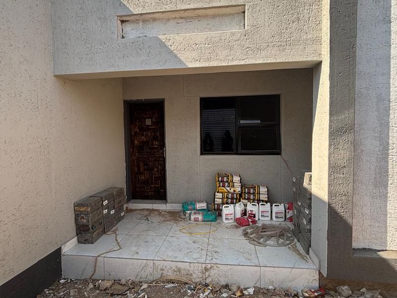Front entrance area of a house under construction, featuring a tiled porch, textured exterior walls, and an installed front door.