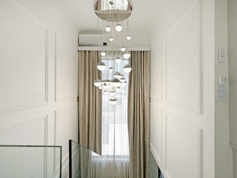 A bright, modern hallway featuring elegant wainscoting, a glass balustrade, and a sophisticated multi-globe pendant light fixture.
