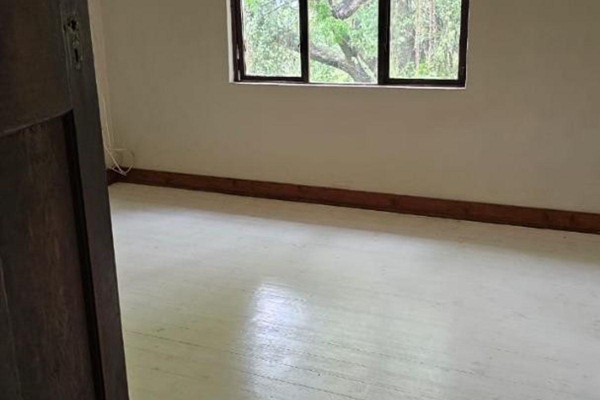An empty bedroom featuring timber flooring, neutral walls, and a wall-mounted air conditioning unit with a view of the surrounding trees.