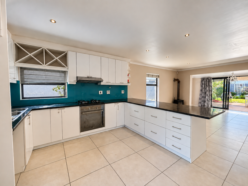 Spacious open-plan kitchen featuring modern white cabinetry, granite countertops, integrated appliances, and tiled flooring, flowing seamlessly into the living area with fireplace.