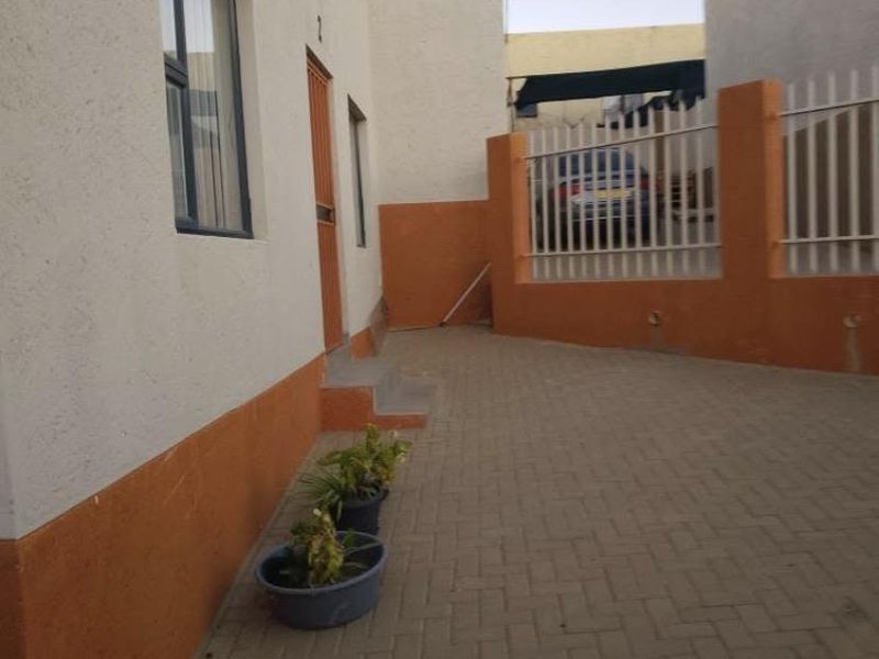 Front exterior view of the townhouse featuring a paved driveway, security gate, and perimeter fencing with plastered wall finishes.